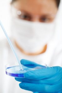 Scientist with face mask using a pipette in a petri dish of blue liquid
