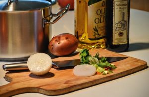 Wooden chopping board with knife, saucepan, ingredients and cooking oil