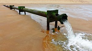 Pipe spilling out water onto sand and into sea